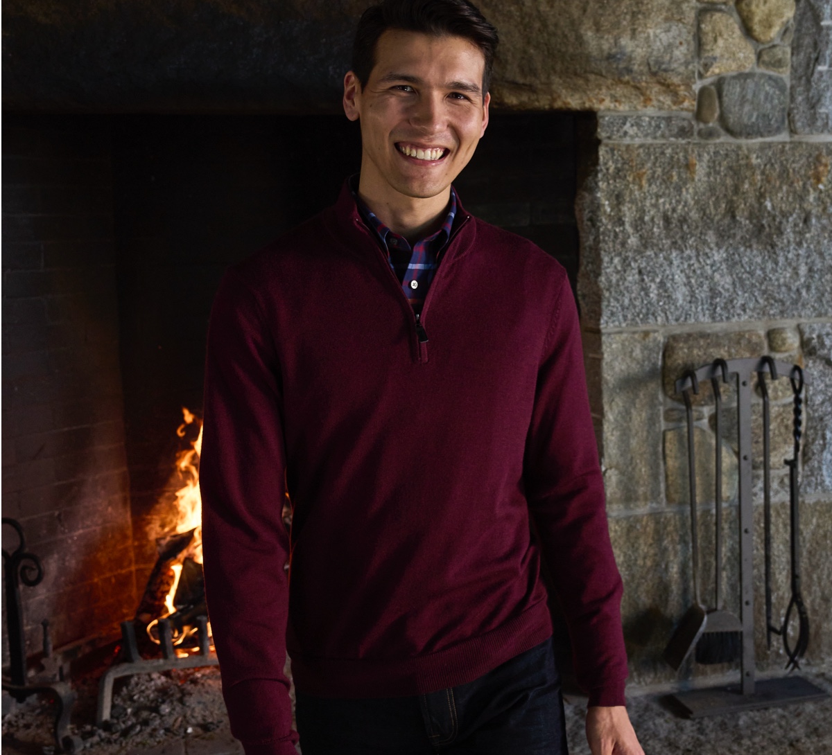 man in burgundy sweater in front of fireplace